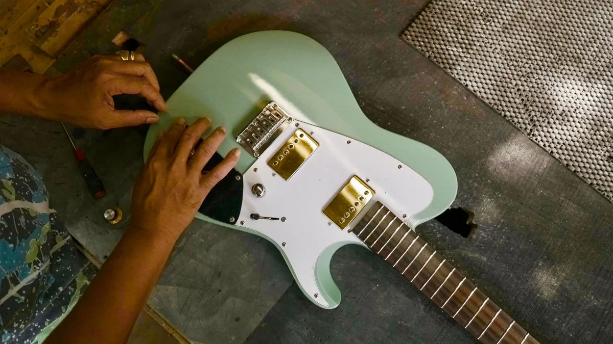 mãos ajustando a ponte de uma guitarra elétrica sobre a bancada, com os selins à mostra