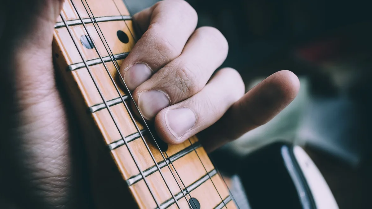 mão fazendo um acorde no braço da guitarra, com os dedos pressionando as cordas