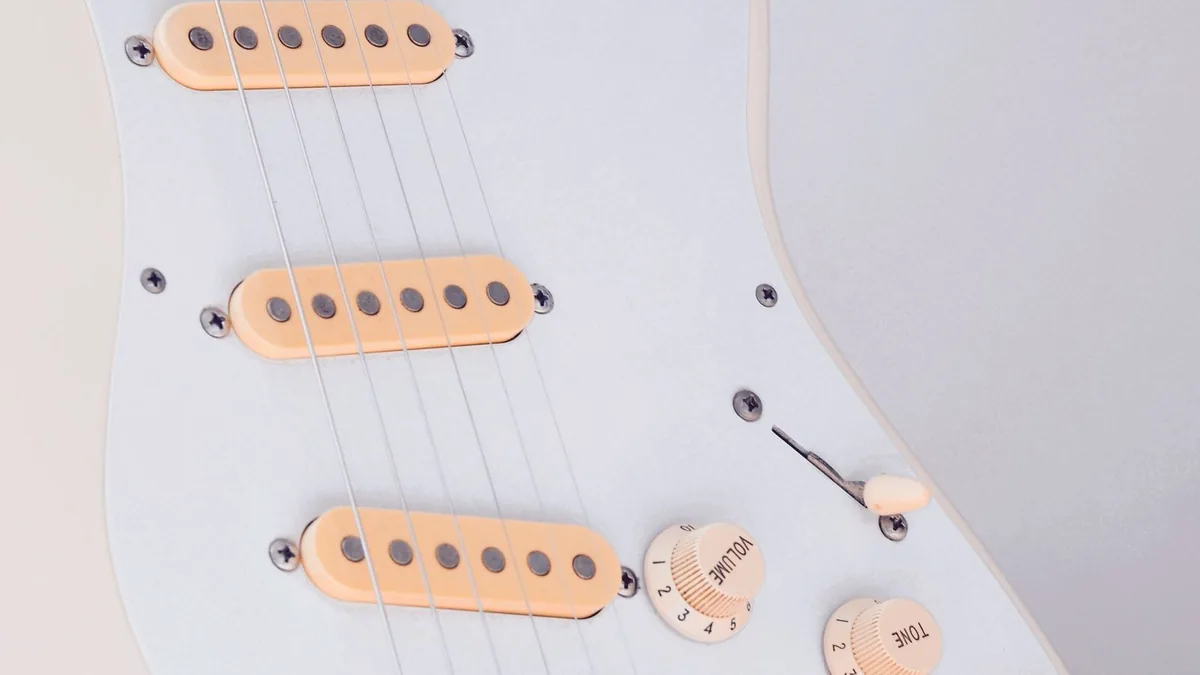guitarra strat com três captadores single coil e pickguard branco, controles de volume e tone visíveis