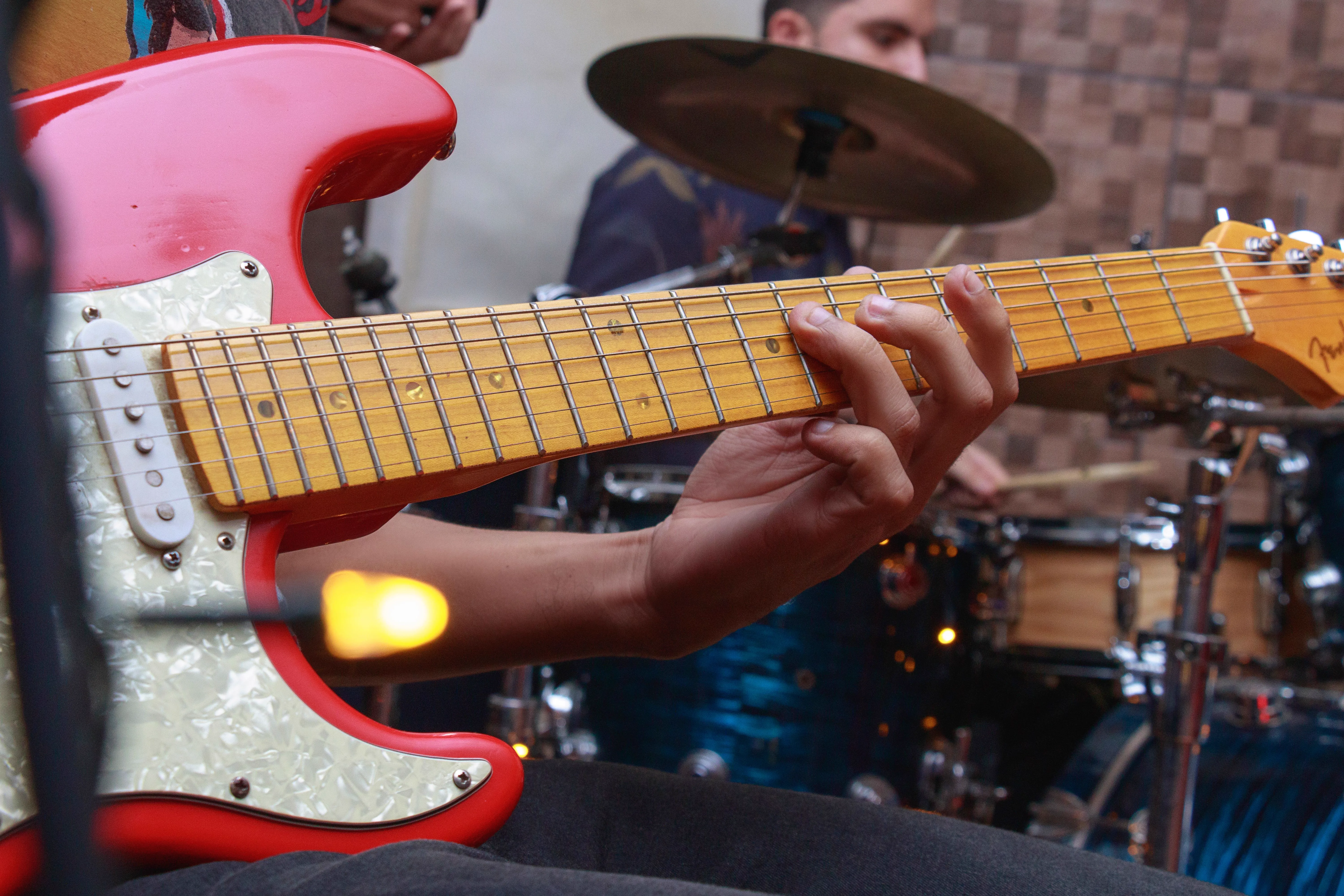 close de guitarrista tocando Stratocaster vermelha ao lado da bateria, em ensaio