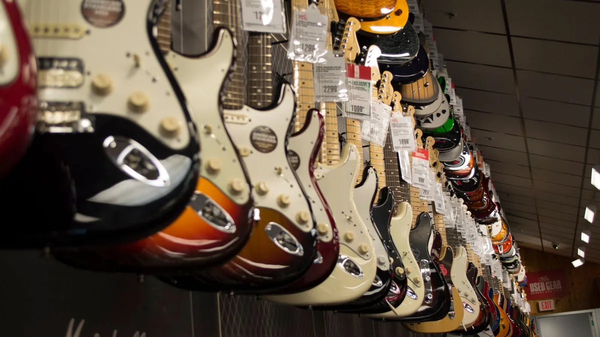 parede de loja com dezenas de guitarras penduradas e etiquetas de preço à vista